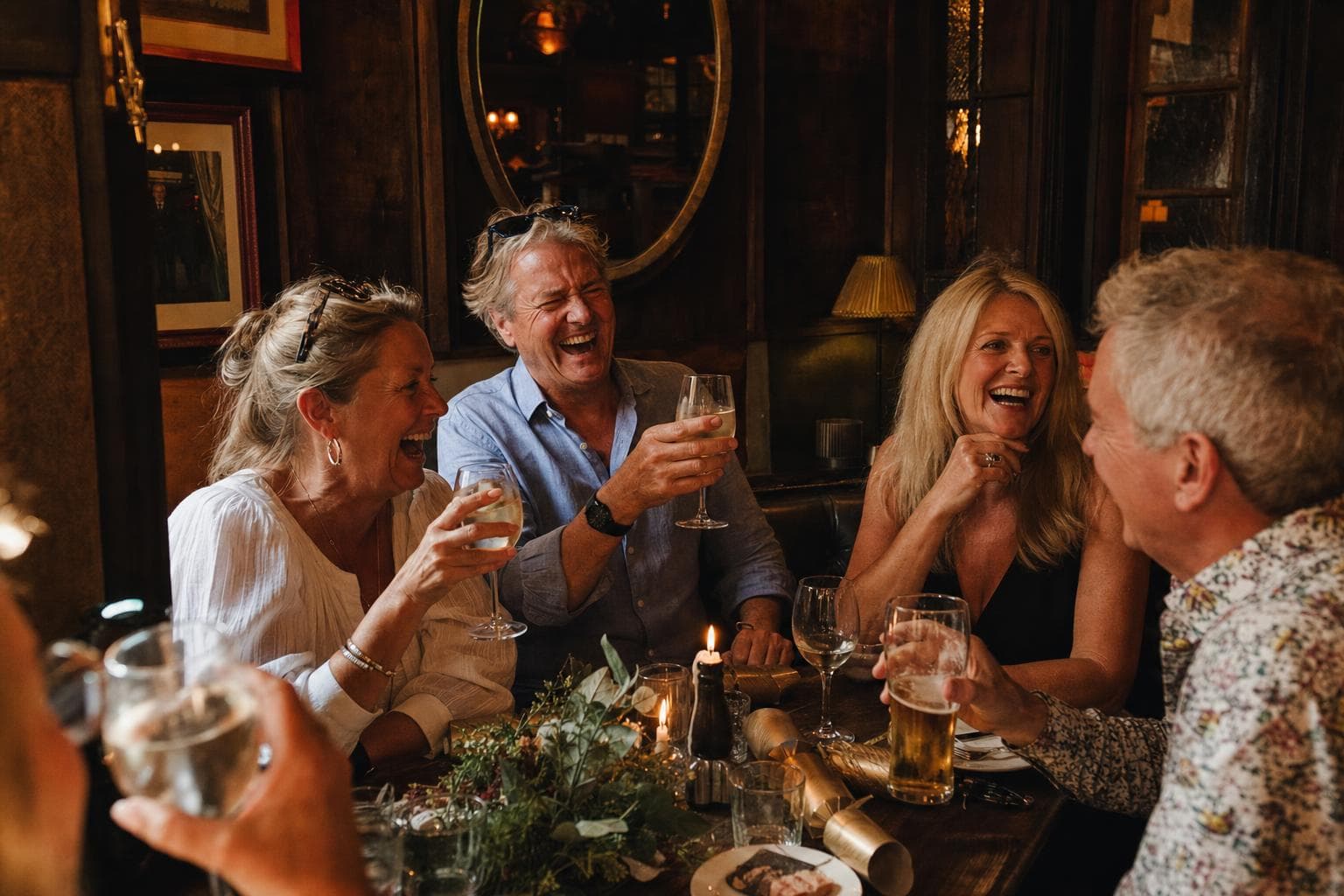 Friends raising glasses at a candlelit pub table set for a festive dinner