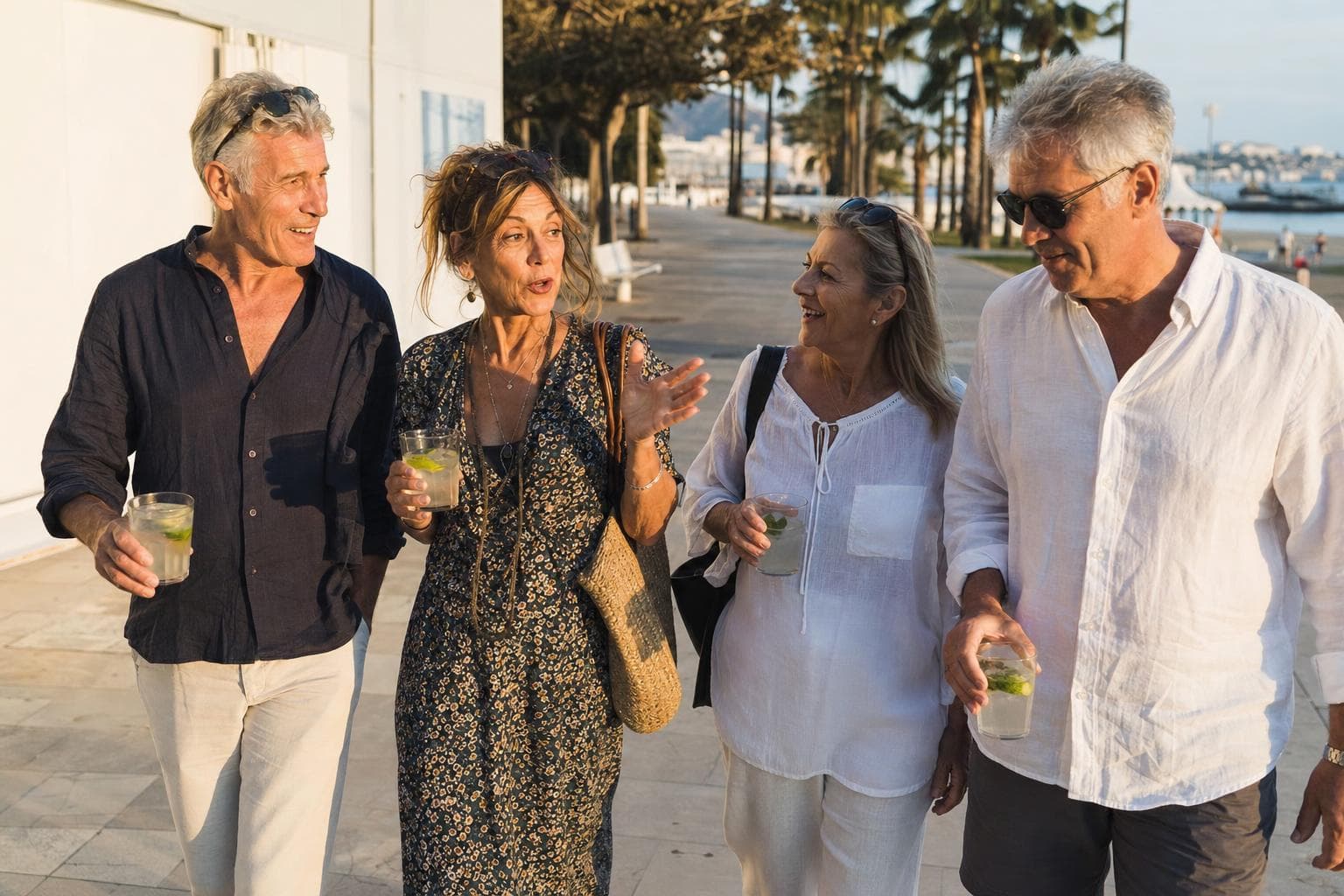 Four friends walking and laughing along a seafront promenade in low evening sun